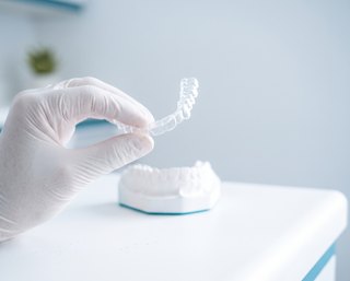 Mão com luva segurando um alinhador ortodôntico transparente ao lado do modelo de gesso